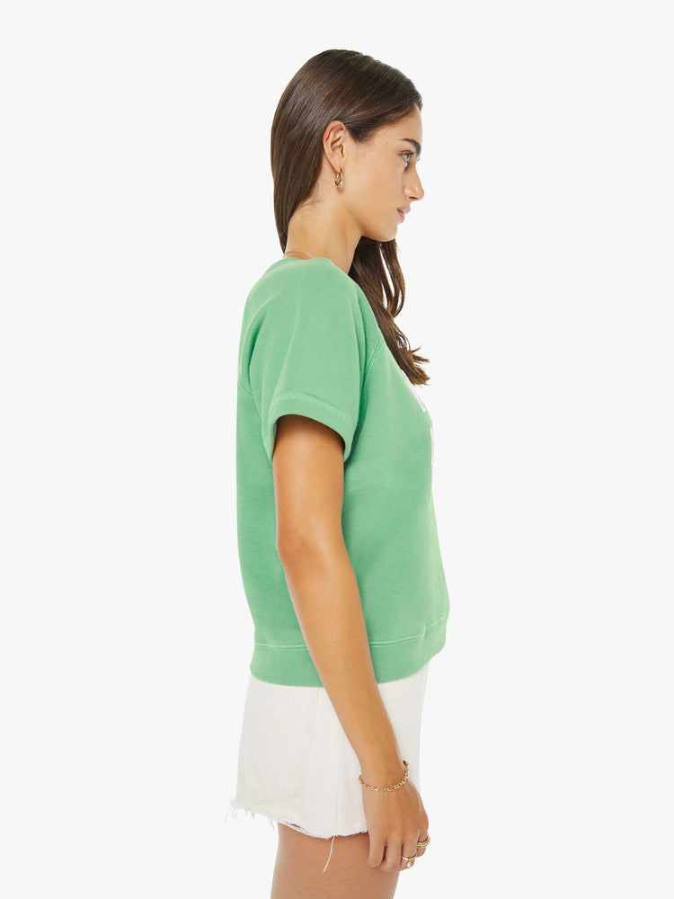 Side view of a woman in a sage green short-sleeve raglan sweatshirt with a white text graphic on the front.