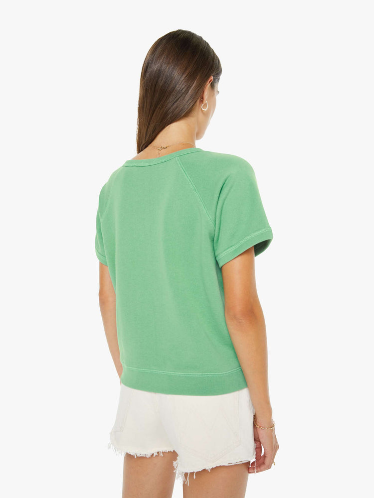 Back view of a woman in a sage green short-sleeve raglan sweatshirt with a white text graphic on the front.