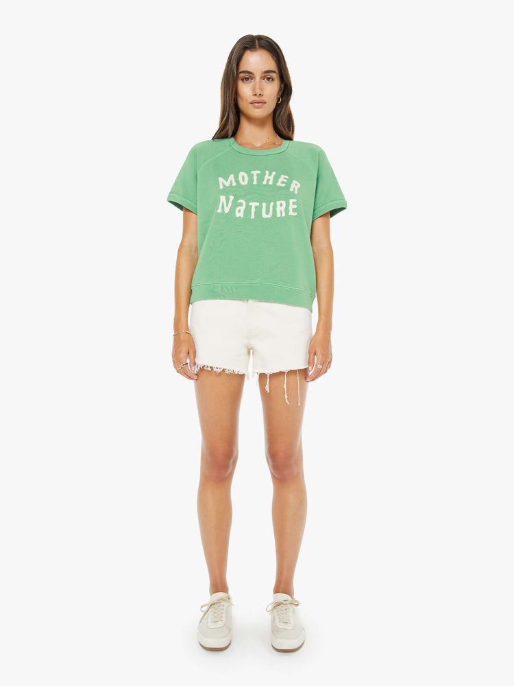 Full body view of a woman in a sage green short-sleeve raglan sweatshirt with a white text graphic on the front.