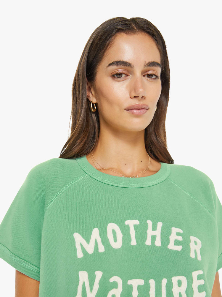 Close up view of a woman in a sage green short-sleeve raglan sweatshirt with a white text graphic on the front.