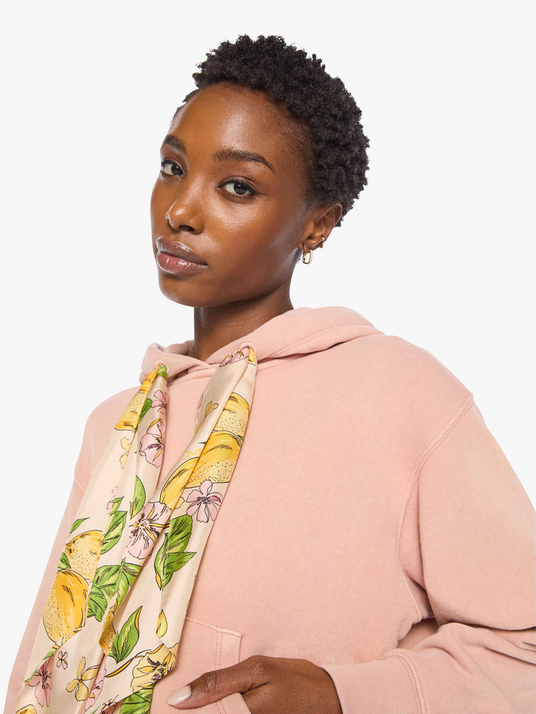 Close up view of a woman in a light pink with colorful scarf drawstring hoodie with drop shoulders, ribbed hems and a front patch pocket.