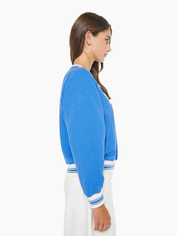 Side view of a woman in a blue sweatshirt with a white text graphic and red stars chainstitched on the front.