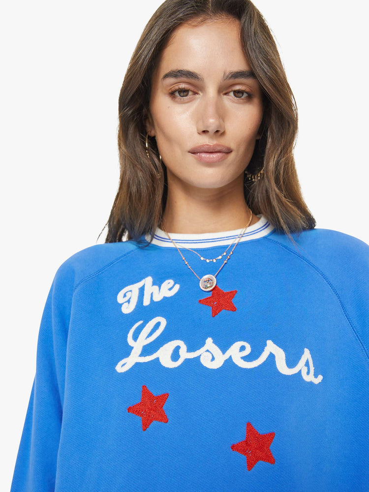 Close up view of a woman in a blue sweatshirt with a white text graphic and red stars chainstitched on the front.