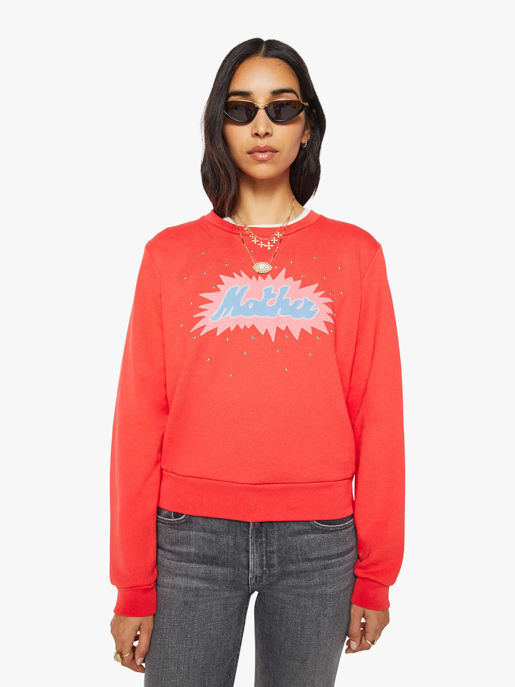 Front view of a woman in a sweatshirt is designed in faded red with a pink and light blue printed graphic and small metal studs throughout.