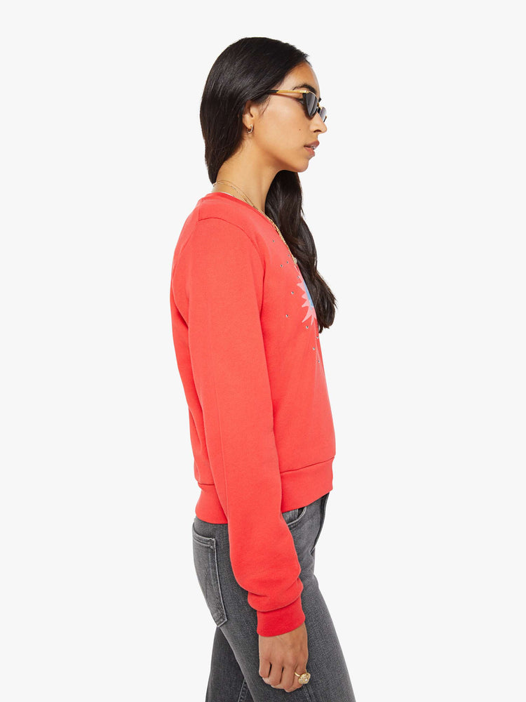 Side view of a woman in a sweatshirt is designed in faded red with a pink and light blue printed graphic and small metal studs throughout.