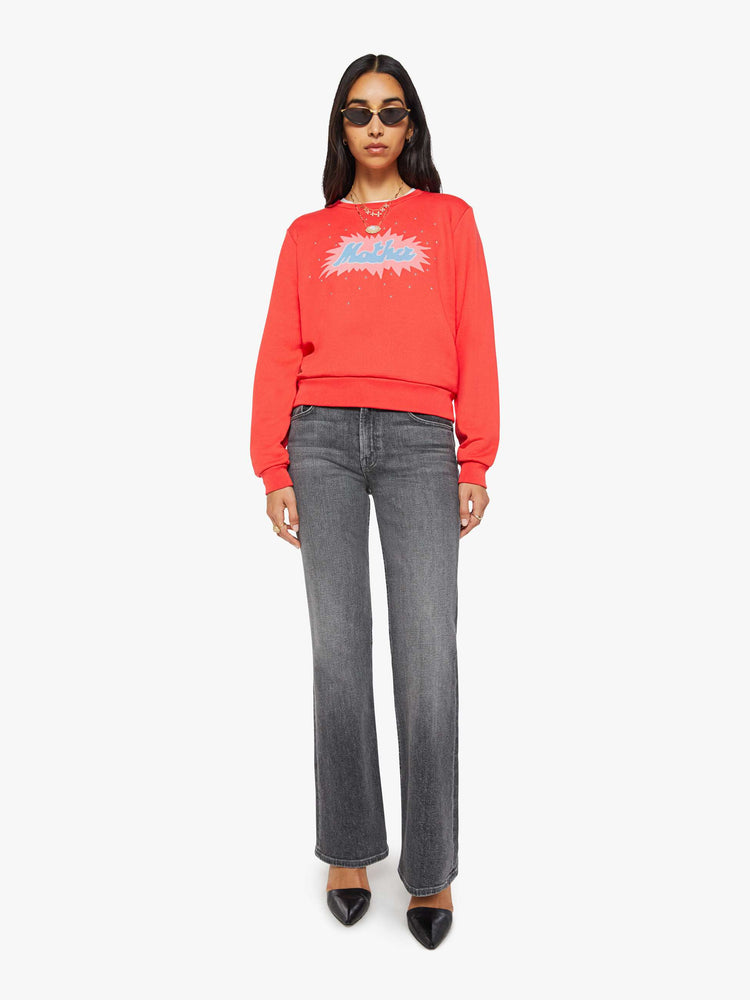 Full body view of a woman in a sweatshirt is designed in faded red with a pink and light blue printed graphic and small metal studs throughout.