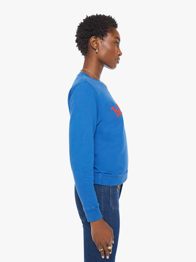 Side view of a woman in a  bright blue with MOTHER's name in red across the chest crewneck sweatshirt with ribbed hems and a loose, comfortable fit.