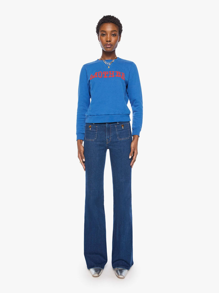 Full body view of a woman in a  bright blue with MOTHER's name in red across the chest crewneck sweatshirt with ribbed hems and a loose, comfortable fit.