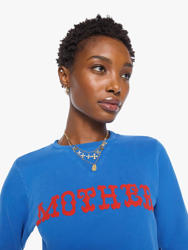 Close up view of a woman in a  bright blue with MOTHER's name in red across the chest crewneck sweatshirt with ribbed hems and a loose, comfortable fit.
