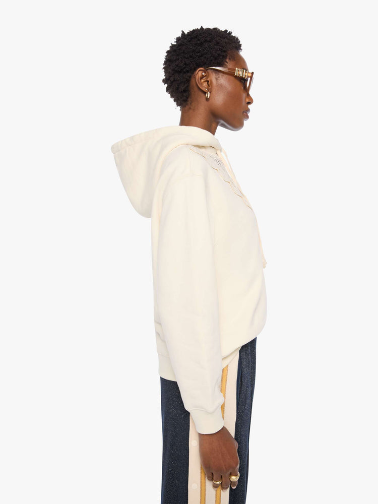 Side view of a woman in an off-white hoodie with an eyelet-embroidered lace detail on the front.