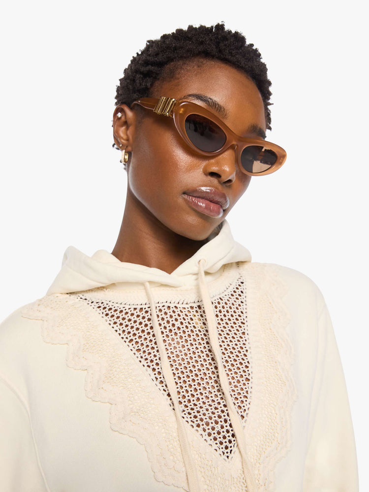 Close up view of a woman in an off-white hoodie with an eyelet-embroidered lace detail on the front.