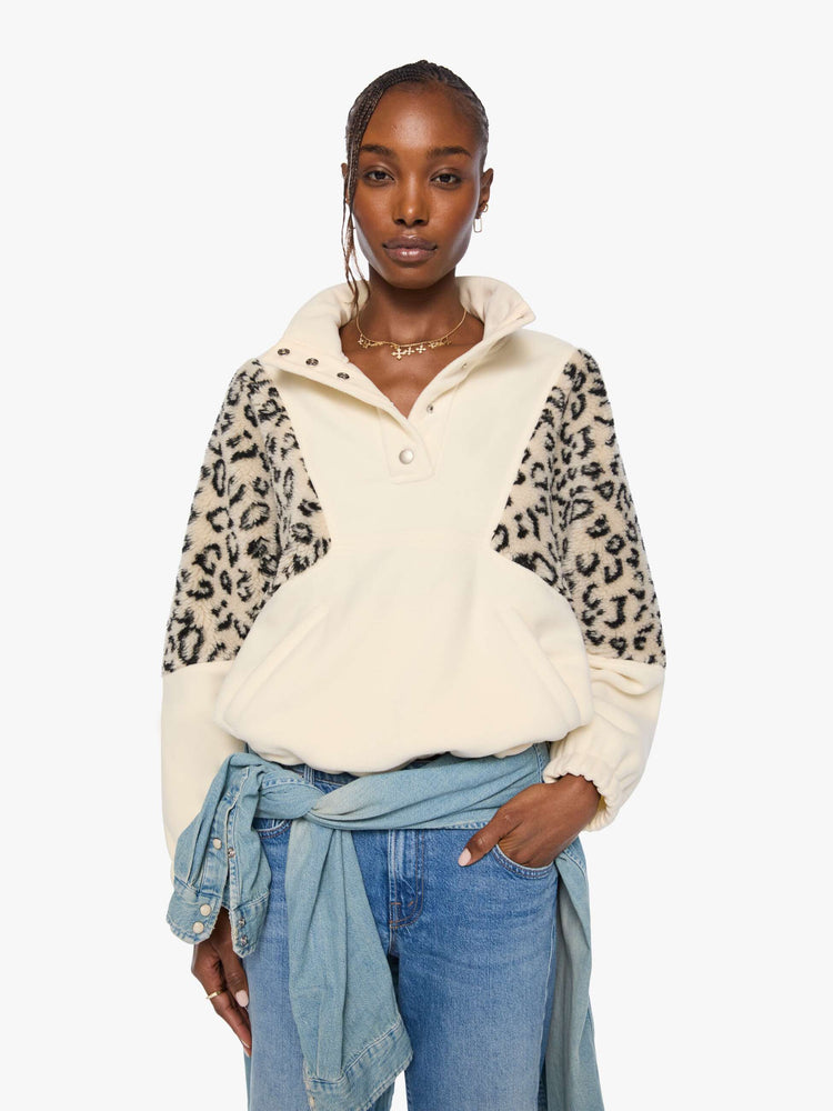 Front view of a woman in a cream with inset cheetah print panels at the shoulders oversized fleece with a buttoned funnel neck, slit pockets and elastic hems. 
