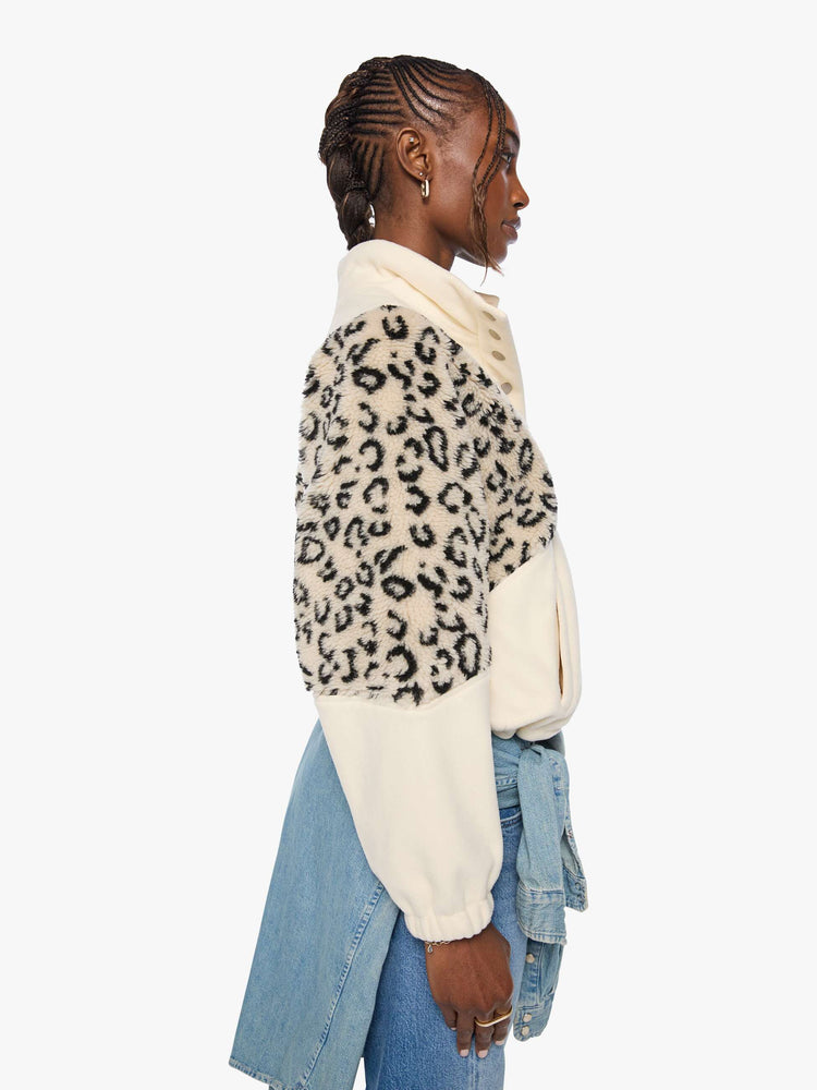 Side view of a woman in a cream with inset cheetah print panels at the shoulders oversized fleece with a buttoned funnel neck, slit pockets and elastic hems. 