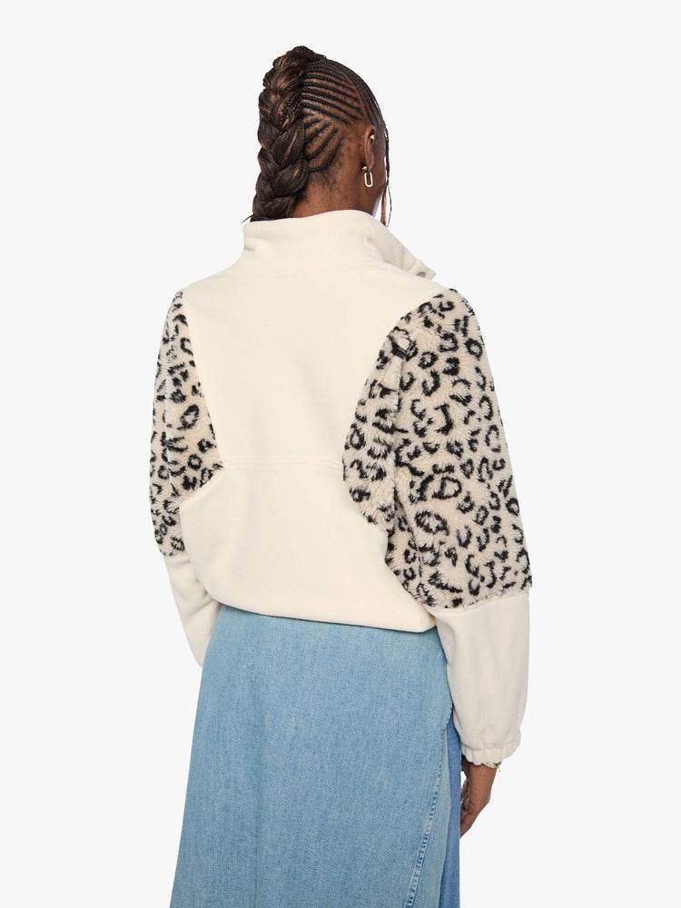 Back view of a woman in a cream with inset cheetah print panels at the shoulders oversized fleece with a buttoned funnel neck, slit pockets and elastic hems. 