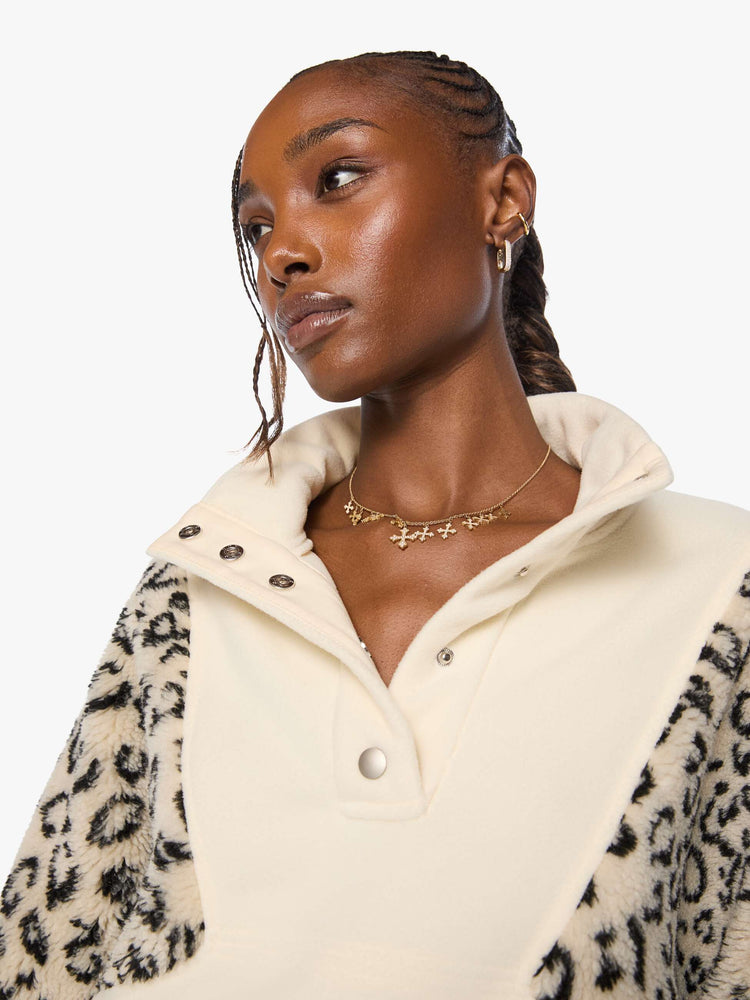 Close up view of a woman in a cream with inset cheetah print panels at the shoulders oversized fleece with a buttoned funnel neck, slit pockets and elastic hems. 
