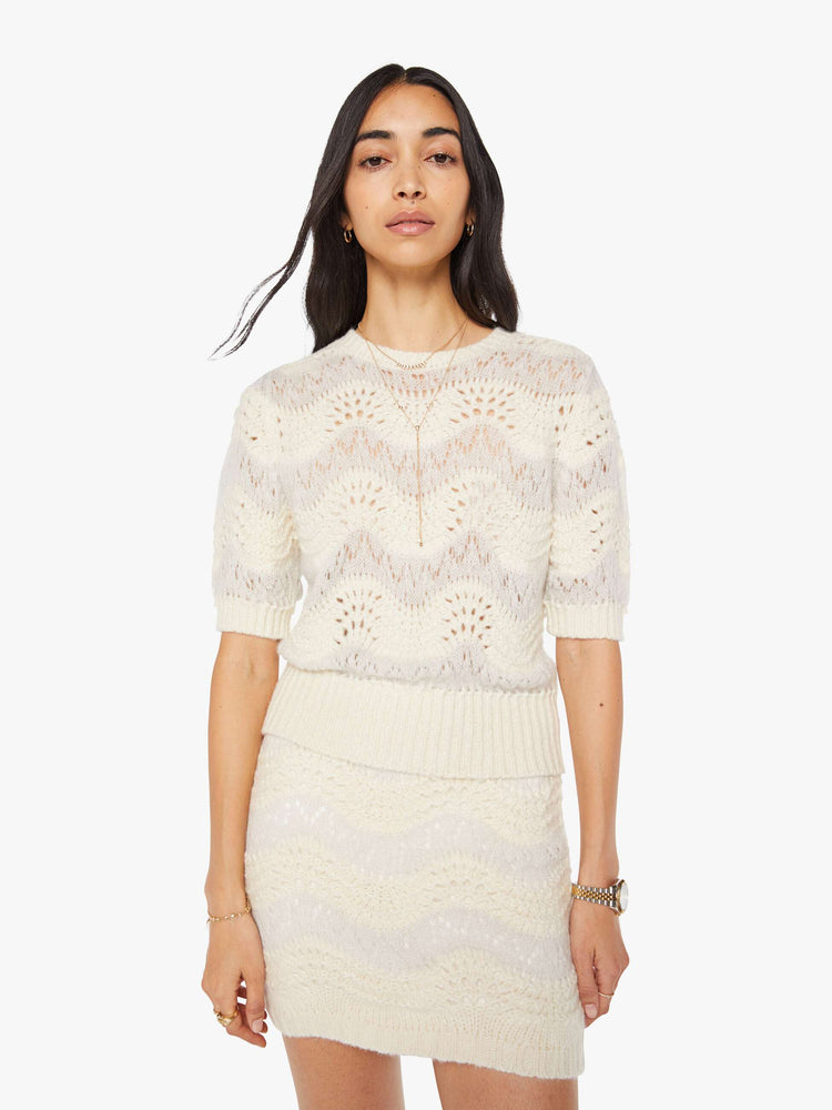 Front view of a woman in a creamy off-white metallic zig-zag stripes knit top with short puffed sleeves, ribbed hems and a slightly cropped fit.