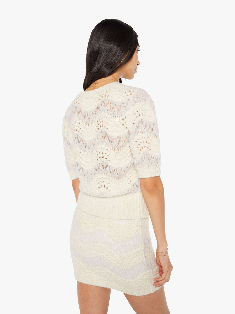 Back view of a woman in a creamy off-white metallic zig-zag stripes knit top with short puffed sleeves, ribbed hems and a slightly cropped fit.