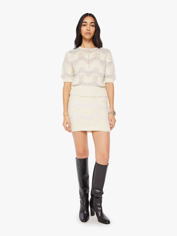 Full body view of a woman in a creamy off-white metallic zig-zag stripes knit top with short puffed sleeves, ribbed hems and a slightly cropped fit.