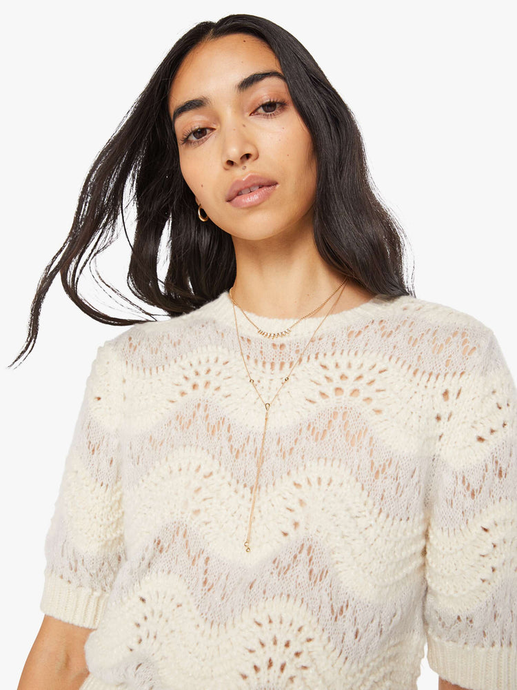 Close up view of a woman in a creamy off-white metallic zig-zag stripes knit top with short puffed sleeves, ribbed hems and a slightly cropped fit.