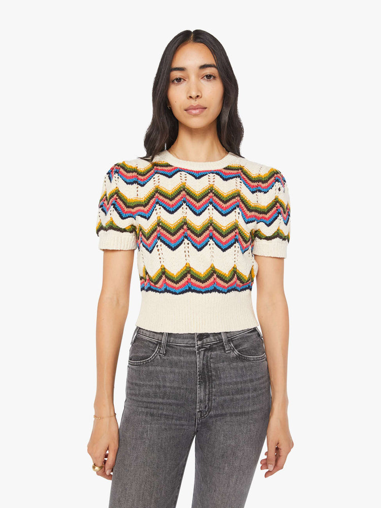 Front view of a woman in an off white knit top with a crewneck, short puffed sleeves, ribbed hems and a slightly cropped fit.