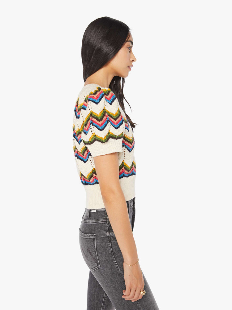 Side view of a woman in an off white knit top with a crewneck, short puffed sleeves, ribbed hems and a slightly cropped fit.