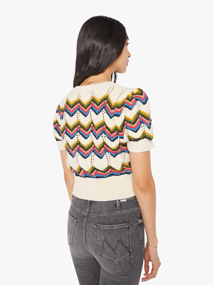 Back view of a woman in an off white knit top with a crewneck, short puffed sleeves, ribbed hems and a slightly cropped fit.