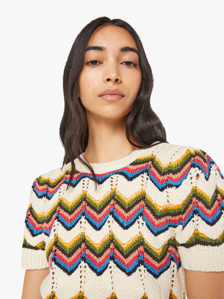 Close up view of a woman in an off white knit top with a crewneck, short puffed sleeves, ribbed hems and a slightly cropped fit.