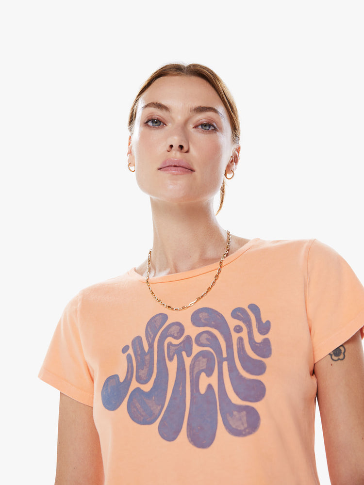 Close up view of a women crewneck with short sleeves, a cropped hem and a slim fit in an orange hue with a lavender graphic.