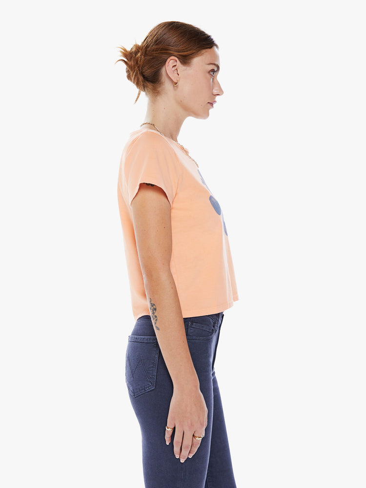 Side view of a women crewneck with short sleeves, a cropped hem and a slim fit in an orange hue with a lavender graphic.