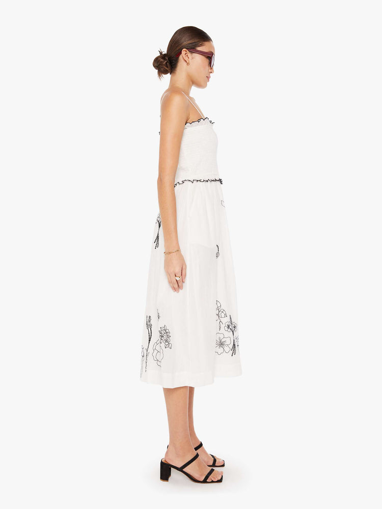 Side view of a womens white dress featuring a full skirt and contrast black embroidery details.
