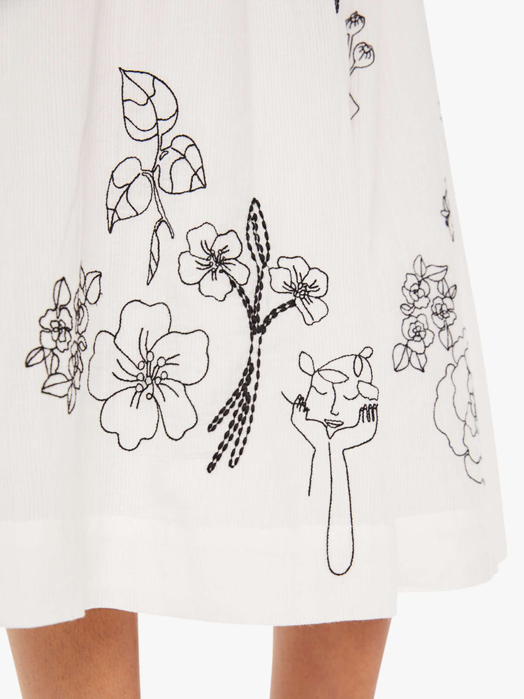 Side close up view of a womens white dress featuring a full skirt and contrast black embroidery details.
