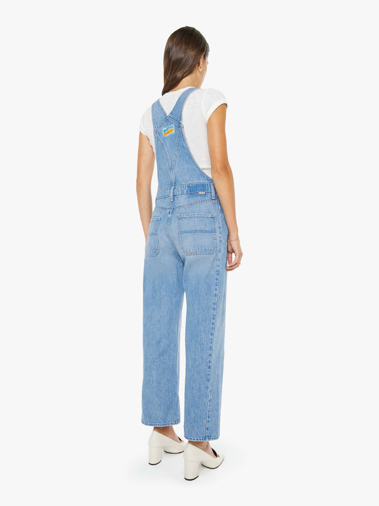 Back view of a woman in a vintage blue denim overalls with adjustable straps, a wide, curved leg, ankle-length inseam and a clean hem. 