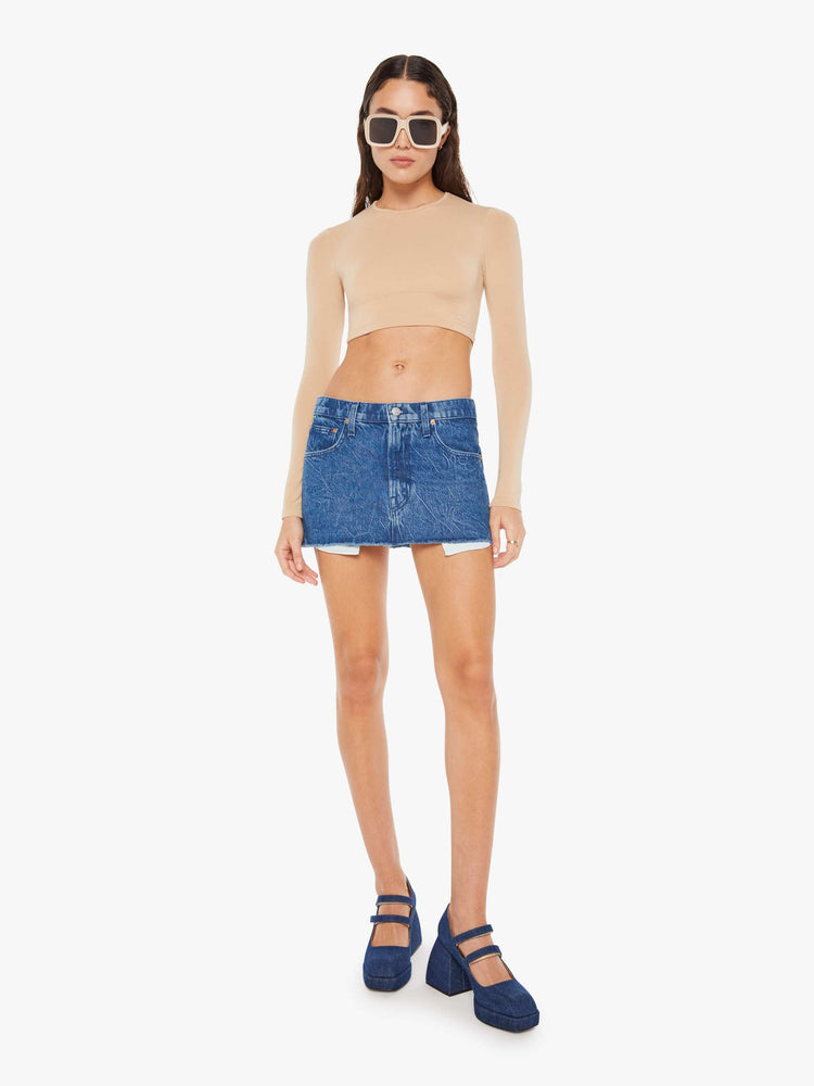Front view of a womens medium blue wash denim mini skirt featuring a raw hem and exposed pockets.