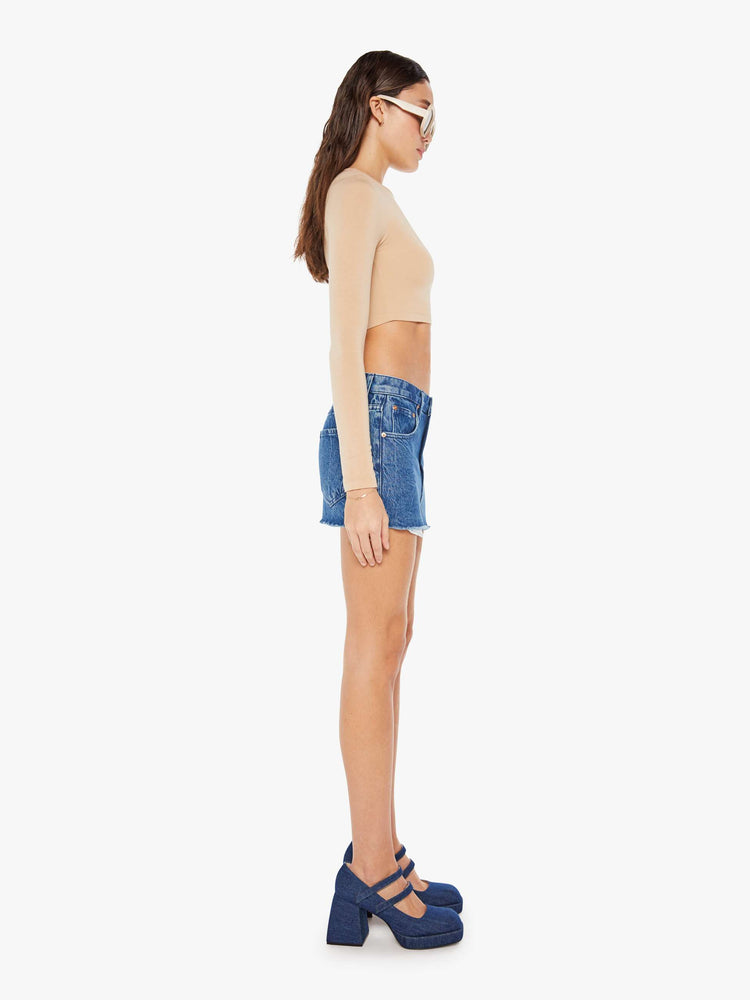 Side view of a womens medium blue wash denim mini skirt featuring a raw hem and exposed pockets.