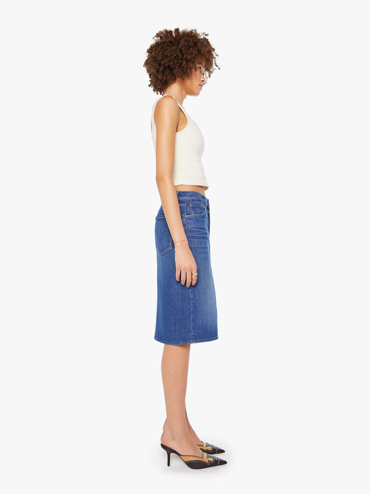 Side view of a woman in mid blue knee- length midi skirt with a zip fly, front slit and clean hem.