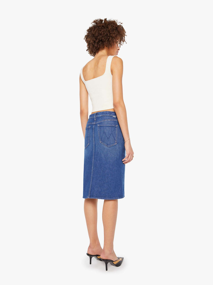 Back view of a woman in mid blue knee- length midi skirt with a zip fly, front slit and clean hem.