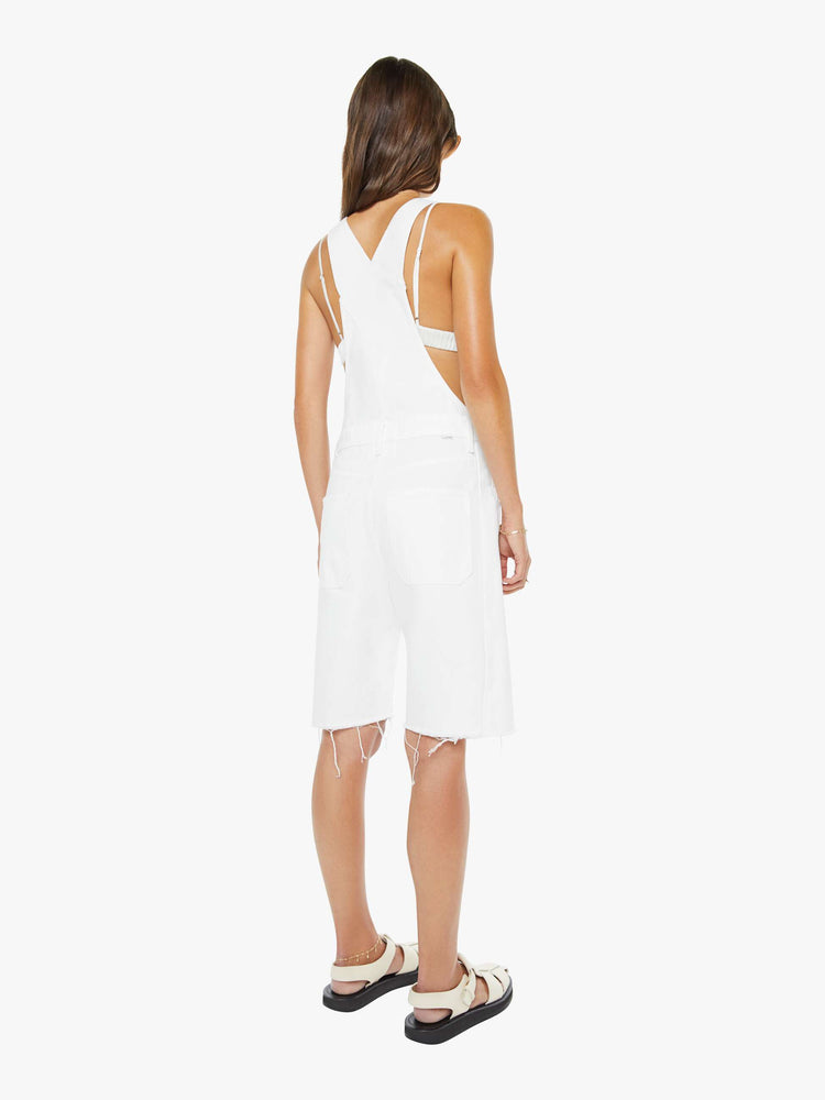 Back view of a woman in a white overalls with a front patch pocket, adjustable straps, a wide leg, knee-length inseam and a frayed hem.