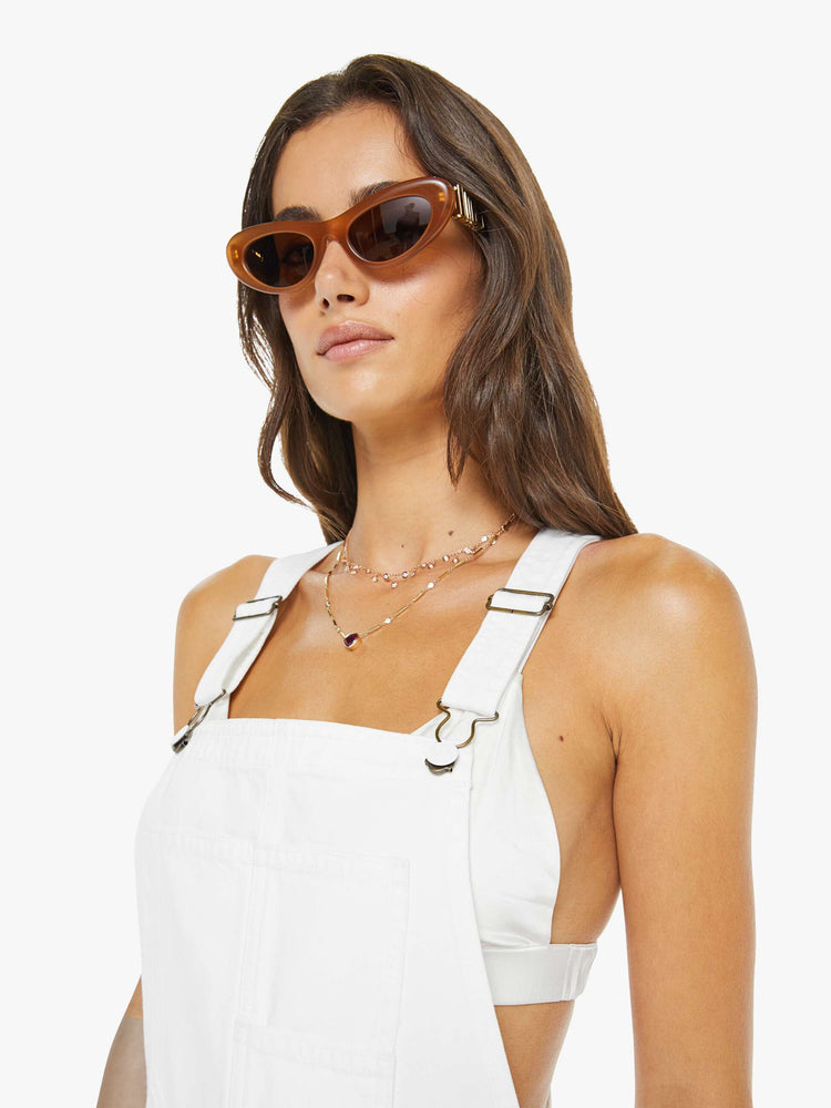 Close up view of a woman in a white overalls with a front patch pocket, adjustable straps, a wide leg, knee-length inseam and a frayed hem.