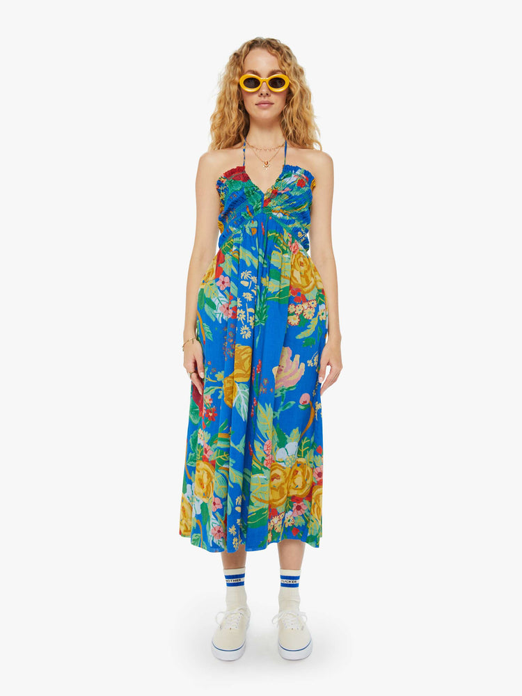 Front view of a woman in a blue tied halter midi dress with an oversized tropical floral print throughout.