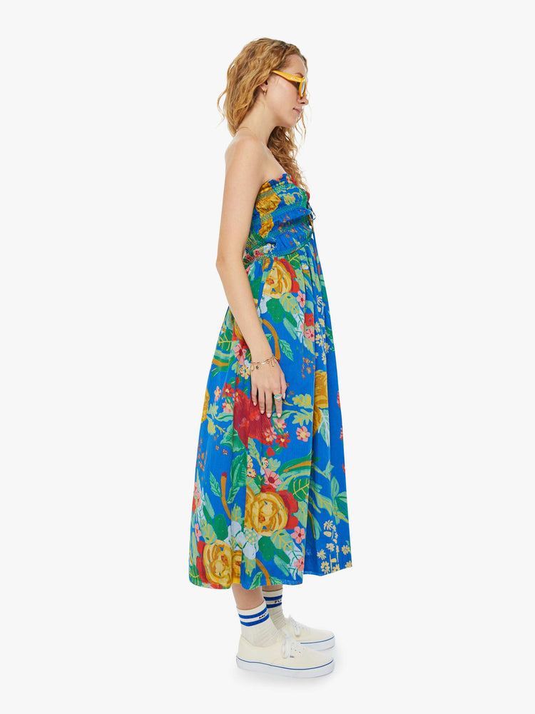 Side view of a woman in a blue tied halter midi dress with an oversized tropical floral print throughout.