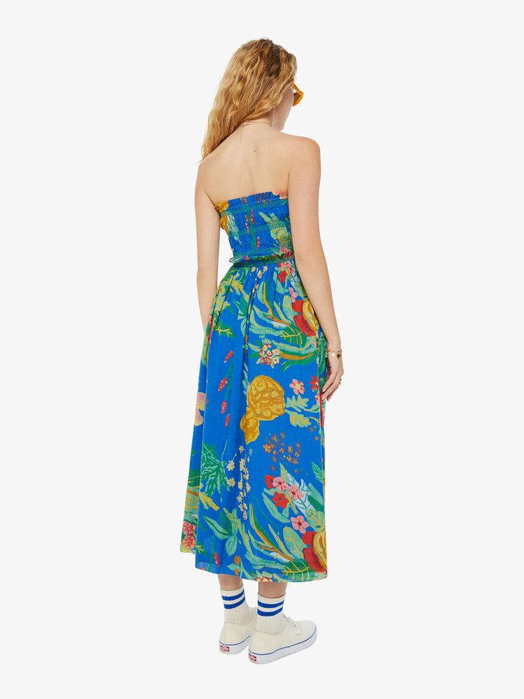 Back view of a woman in a blue tied halter midi dress with an oversized tropical floral print throughout.
