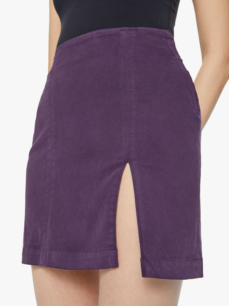 Close up view of a woman high-waisted mini skirt with a thigh slit, narrow fit and a side zip closure in a blackberry-purple.