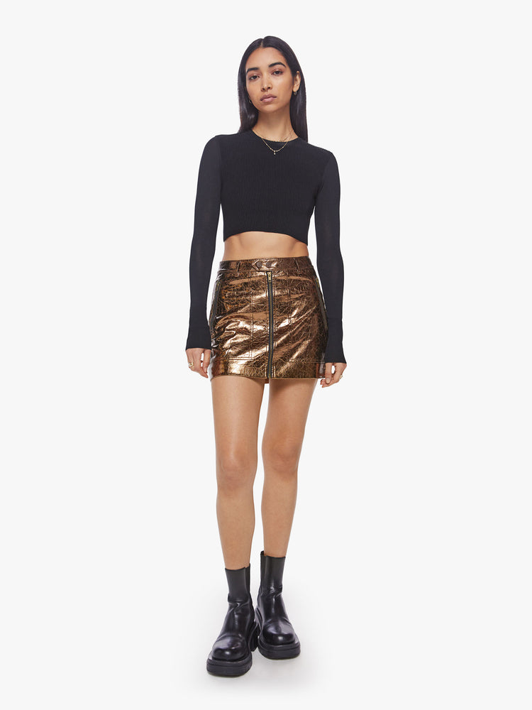 Front view of a woman high shine metallic golden hue zip-up mini skirt with a high rise, buttoned waistband and patch pockets.
