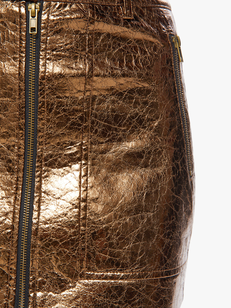 Close up view of a woman high shine metallic golden hue zip-up mini skirt with a high rise, buttoned waistband and patch pockets.