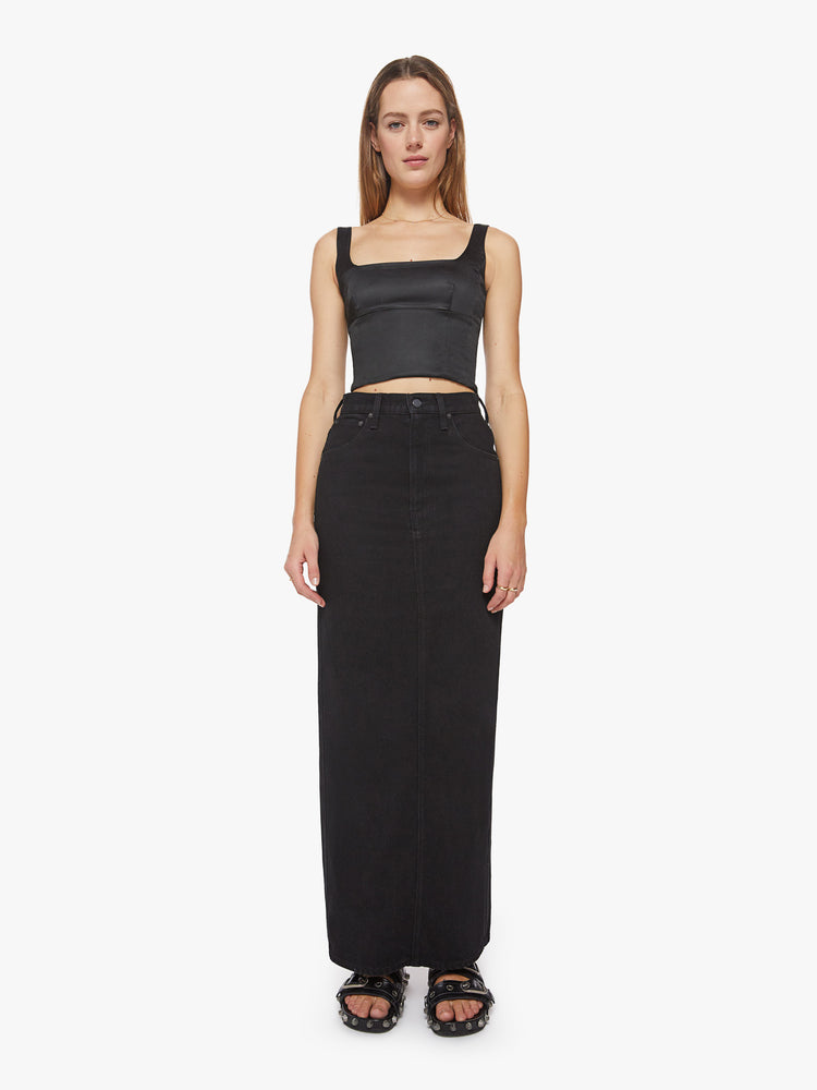 Front view of a woman black denim skirt with a high rise, floor-length hem and a back slit. 