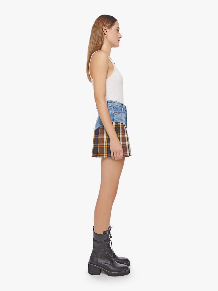 Side view of a woman half denim and half navy, orange and brown plaid mini skirt with a high rise, raw edge and pleated bottom.