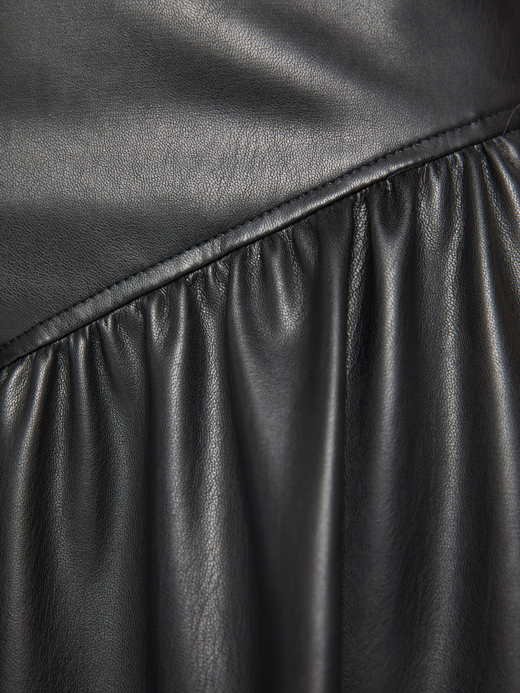 Close up view of a woman midi skirt fitted at the waist with diagonal seams and ruffles for a flowy fit in a black faux leather.