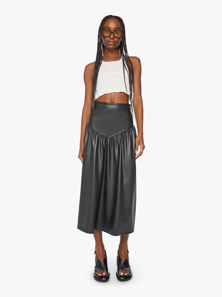 Front view of a woman midi skirt fitted at the waist with diagonal seams and ruffles for a flowy fit in a black faux leather.