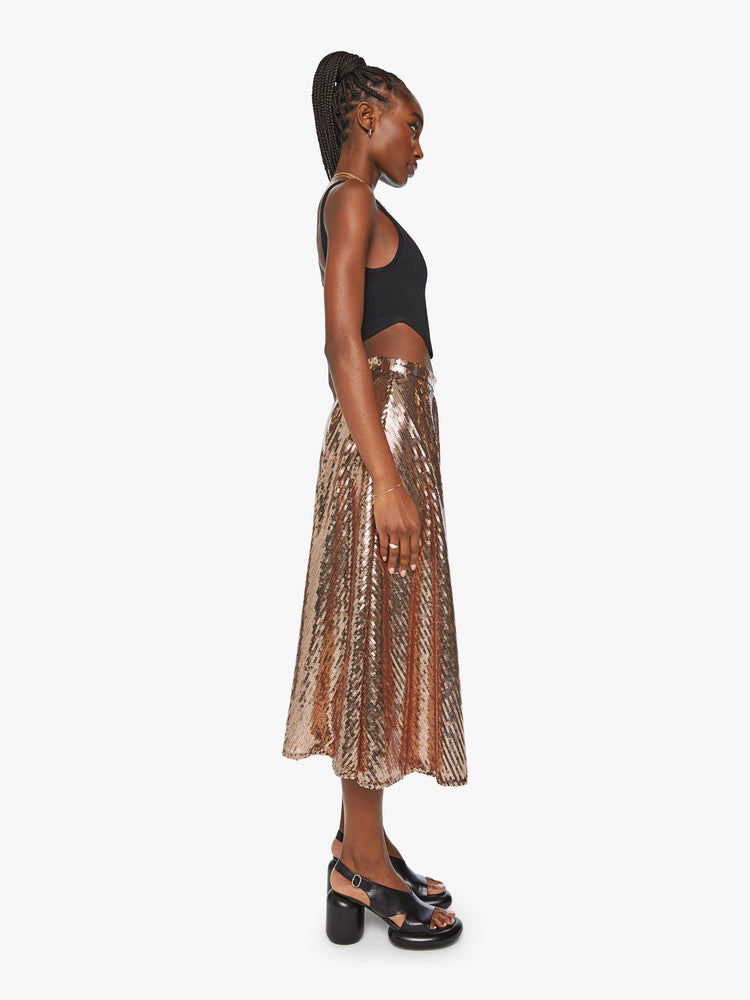 Side view of a woman flowy midi skirt with a high rise, loose fit and calf-grazing hem in a metallic gold sequins throughout.