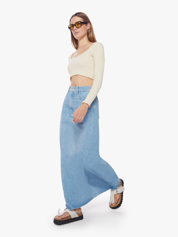 Walking view of a woman high-waisted denim maxi skirt features a zip fly, loose A-line fit and a long hem in a light blue wash.